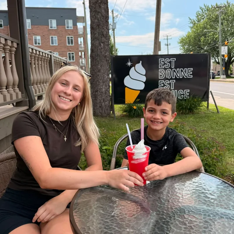Une jeune femme et un garçon sur la terrasse, une slush à la main, devant l'affiche « Est bonne, est douce »