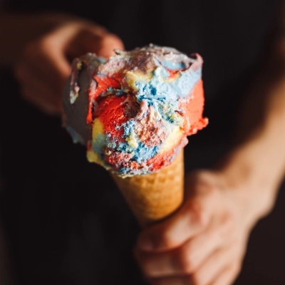 Cornet de crème glacée multicolore tenu dans une main